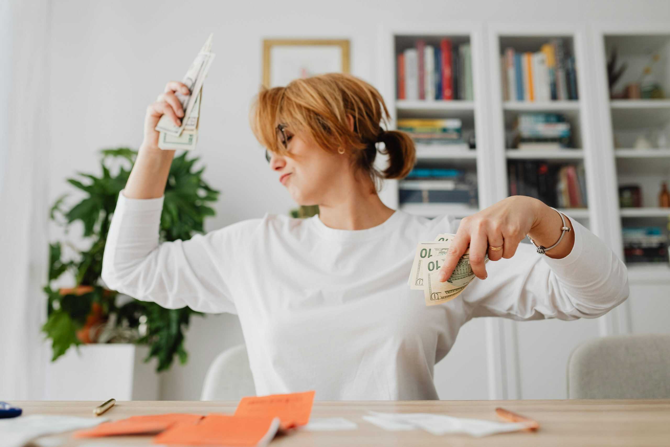 Smiling woman celebrating how to stick to a budget results with cash in hand at her desk, symbolizing budgeting success and financial confidence.