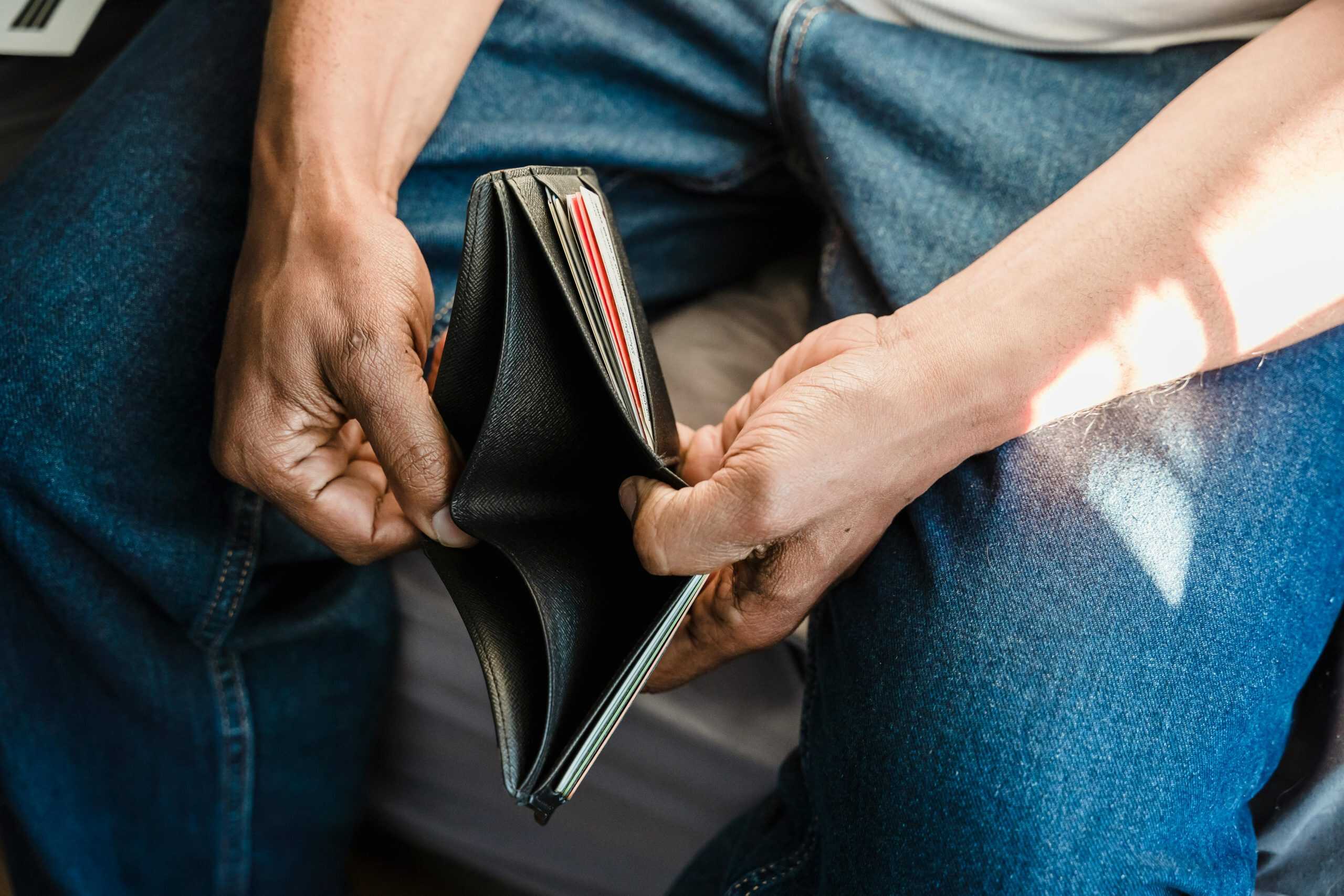 A person sitting down and holding an empty wallet, symbolizing the stress and frustration of budgeting when money is tight.