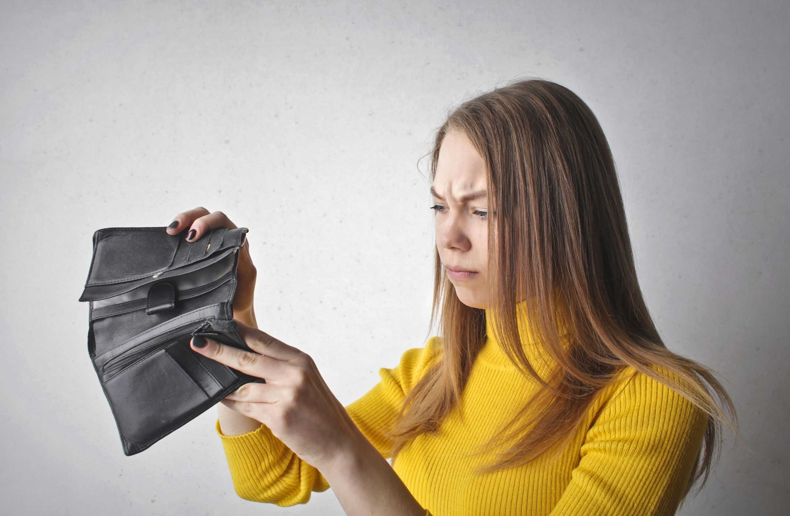 Woman in a yellow sweater looking concerned as she checks her empty wallet and wonder why her budget isn't working.