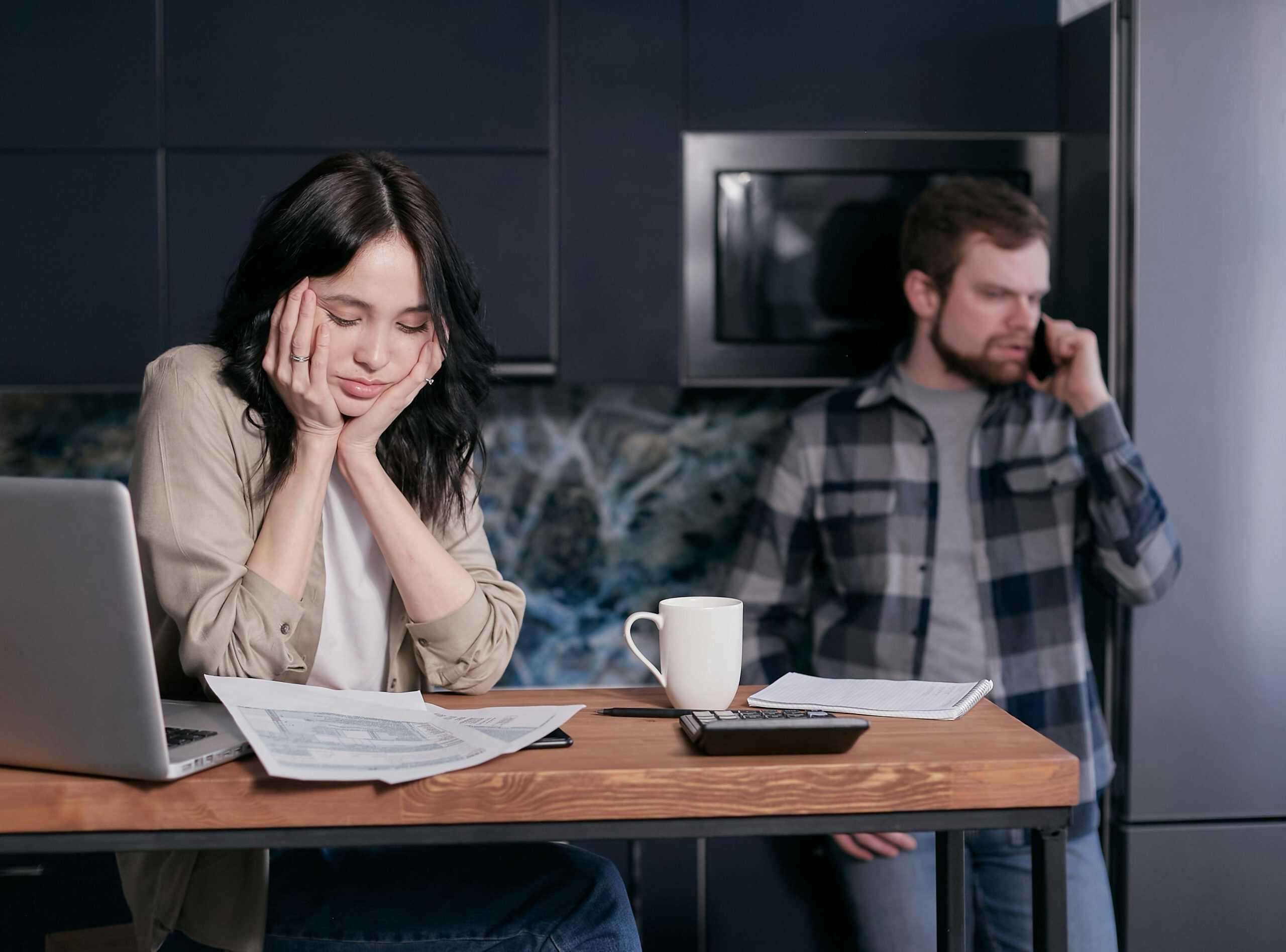 A stressed couple reviewing bills at a kitchen table while one person is on the phone—illustrating the emotional toll of dealing with debt collectors