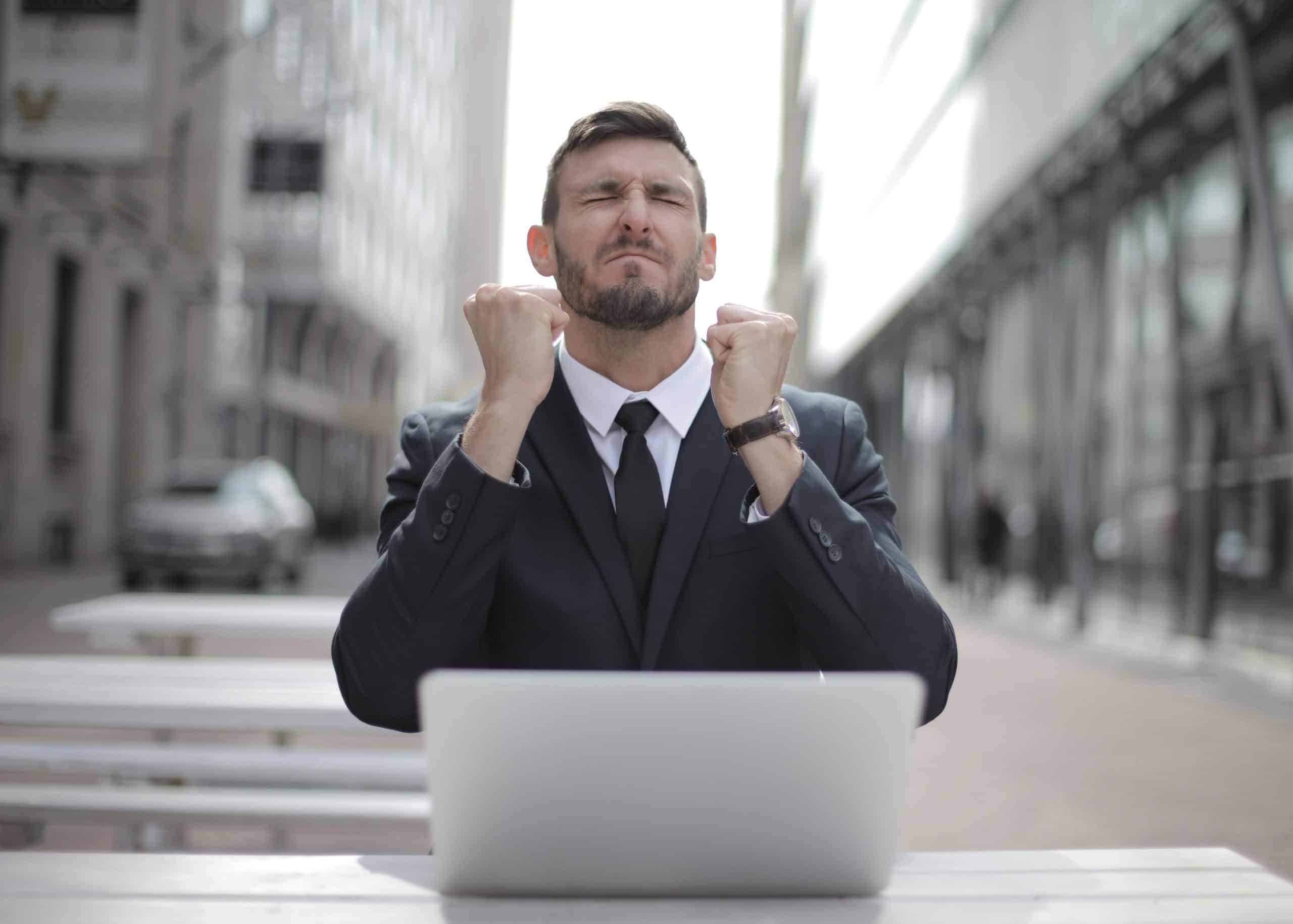 Man in business suit celebrating financial success at laptop, symbolizing the freedom and relief that comes from learning how to automate savings and bill payments.